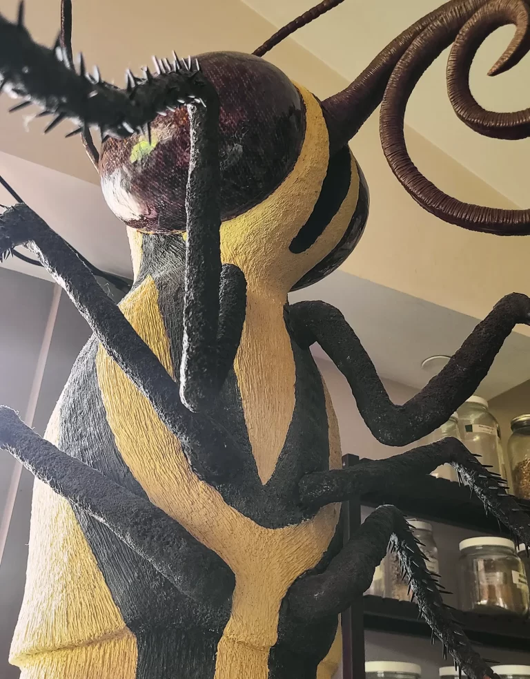 Enormous suspended caterpillar sculpture displaying characteristic warning coloration stripes and segmented body with extending prolegs. Museum installation transforms tiny larval form into monumental presence with organic textures and dynamic spatial composition.