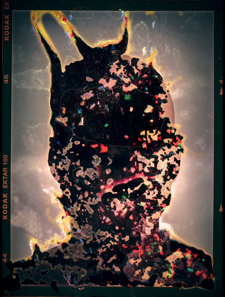 Biologically-processed photographic artwork.Silhouette displays triumphant pose with luminous aureate border and multicolored biological transformations including emerald growth, crimson reactions, and azure mineral deposits from earthbound decomposition processes.