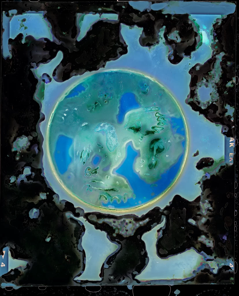 Alternative photographic process artwork featuring luminous sphere with aureate border displaying azure and emerald fluid patterns. Underground film burial method produces celestial composition with geographical formations surrounded by volcanic-textured decomposed matter and film edge markings.RetryClaude can make mistakes. Please double-check responses.