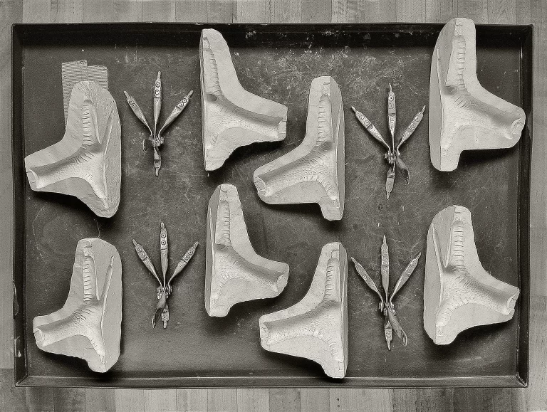 Museum preparation tray displaying multiple sculptural dodo feet reproductions with characteristic robust three-toed design and prominent claws. Systematic arrangement shows various completion stages and individual anatomical elements for scientific reconstruction of extinct bird species.