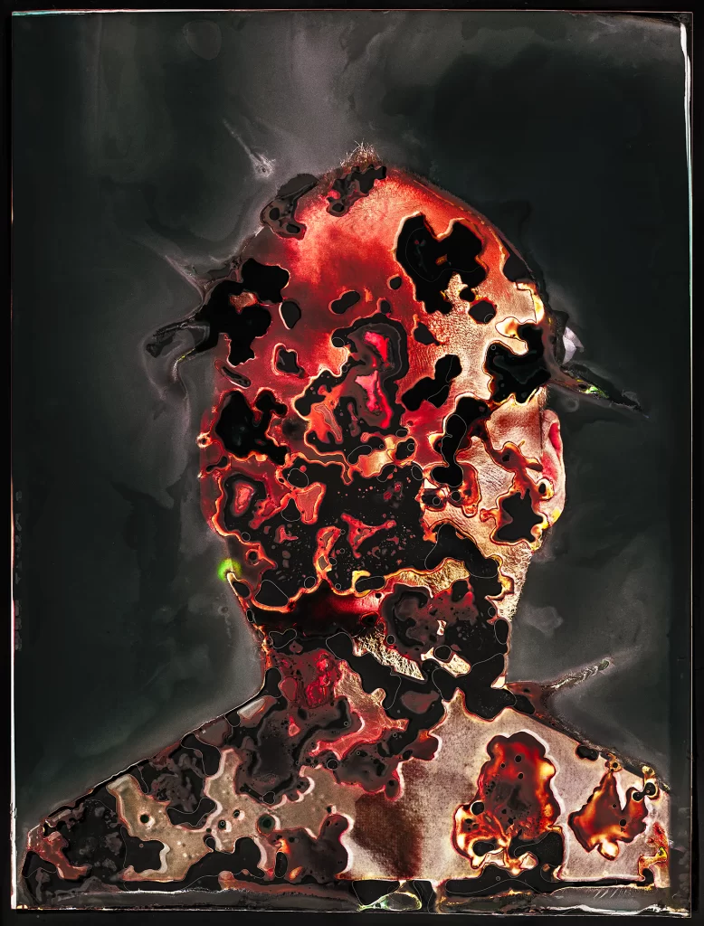 Self-portrait on color negative film created through biological imaging showing frontal bust with internal luminosity effect. Image displays intense crimson and golden coloration with black organic flows, metallic chemical reactions, and sculptural voids from extended soil burial processing creating molten appearance.